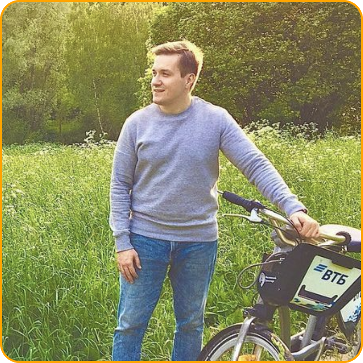 Picture of Sergey standing in a green field with tall grass next to a bicycle