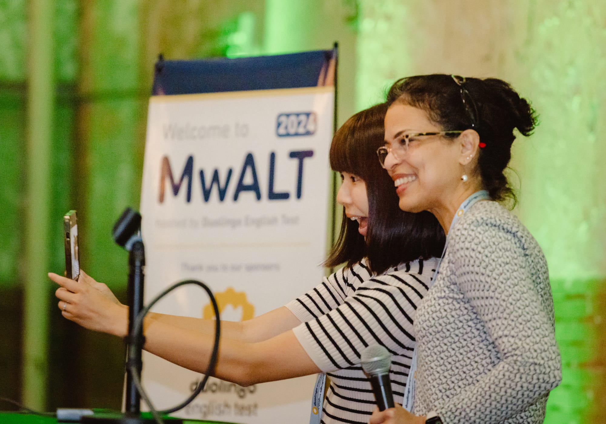 Two women on a stage, smiling and posing for a selfie. 