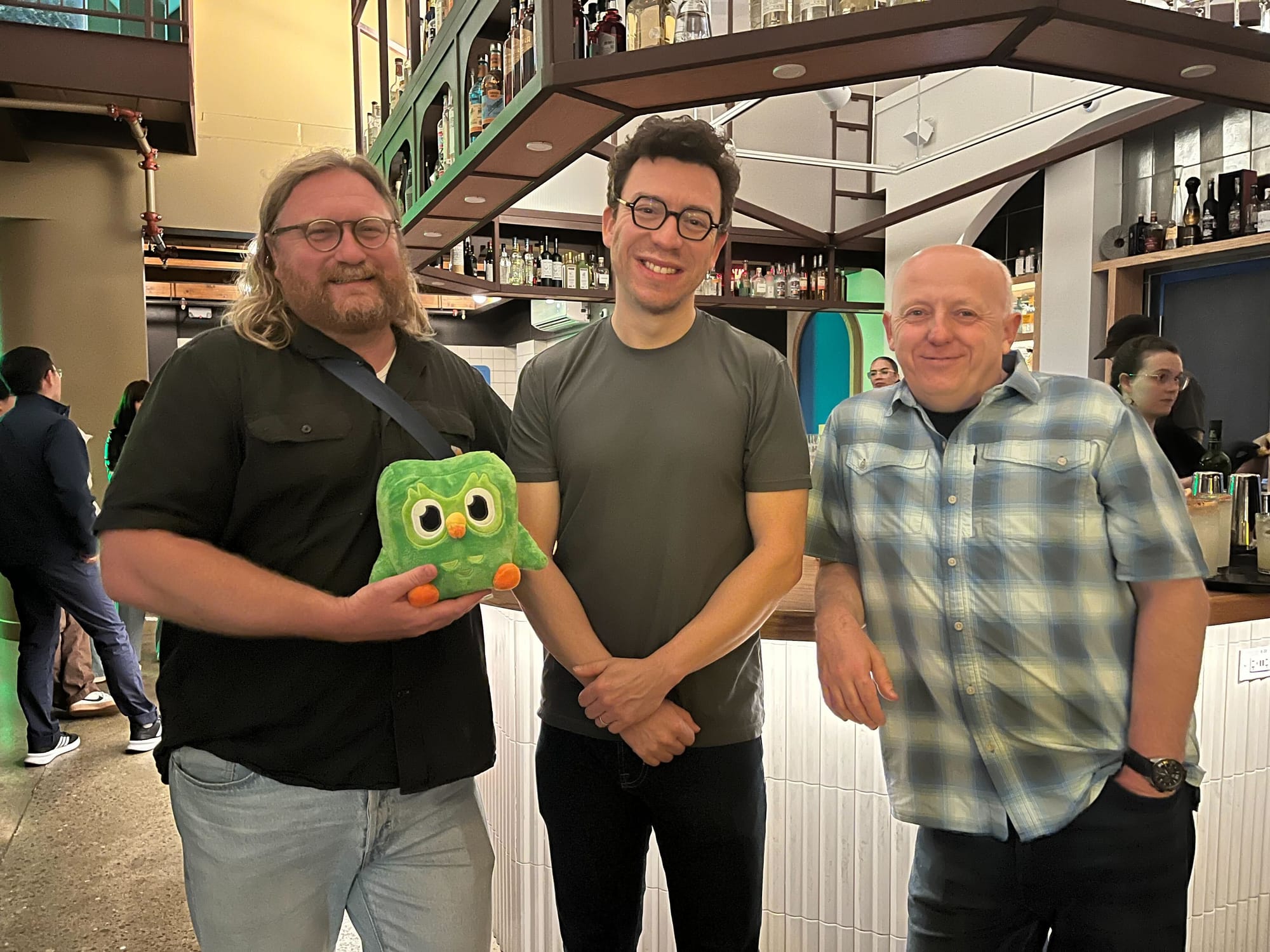 Three men standing against a bar, smiling, and facing the camera