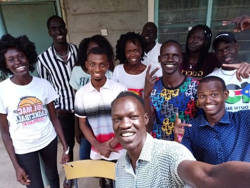 Several students posing together smiling. The man in the front's arm is extended, taking a selfie.