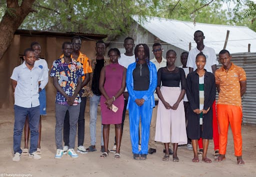 Fourteen students standing outside in a line, facing the camera. 