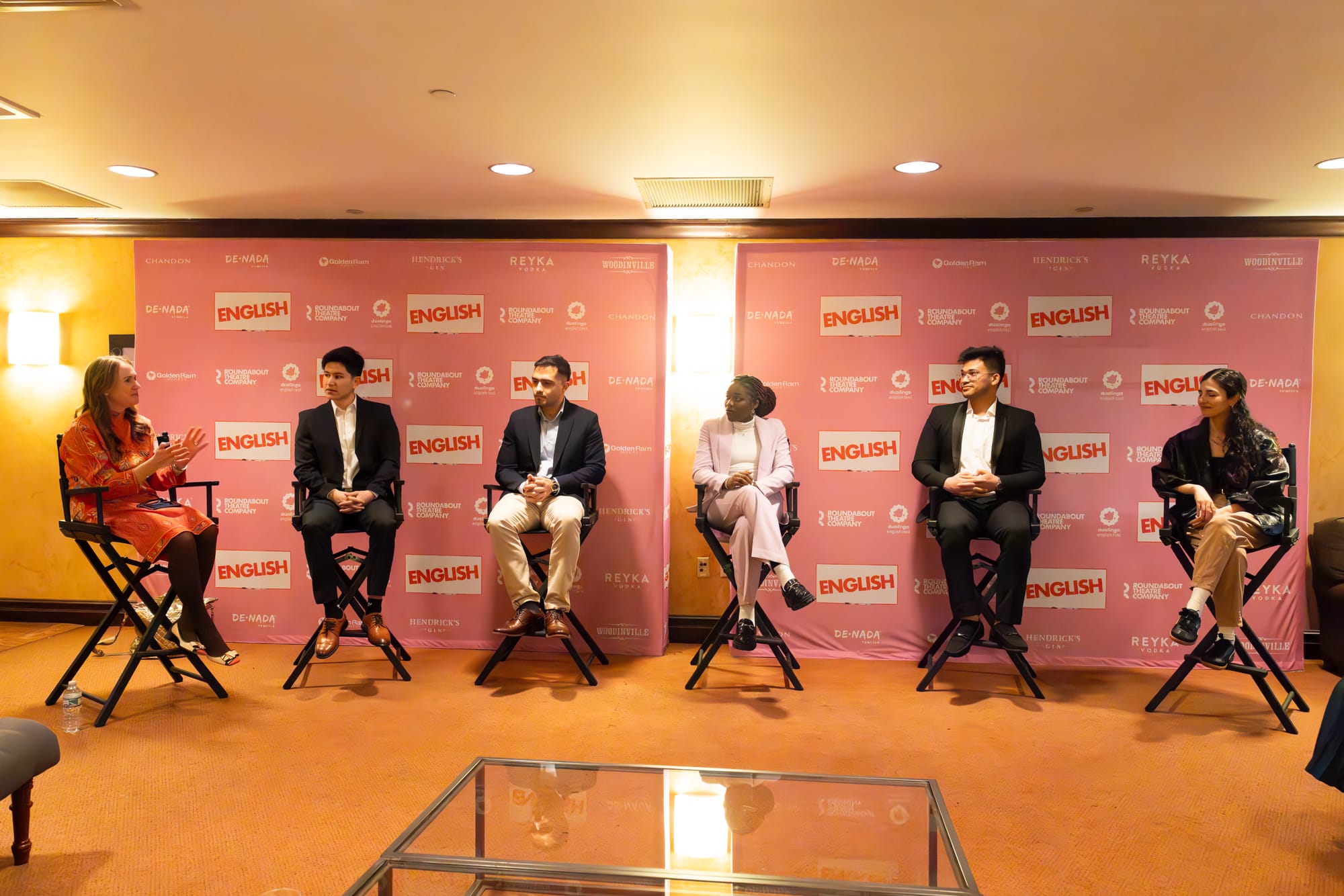 Six people sitting on directors chairs for a panel discussion. Behind them is a pink step and repeat, printed with the words "ENGLISH" and "Duolingo English Test"