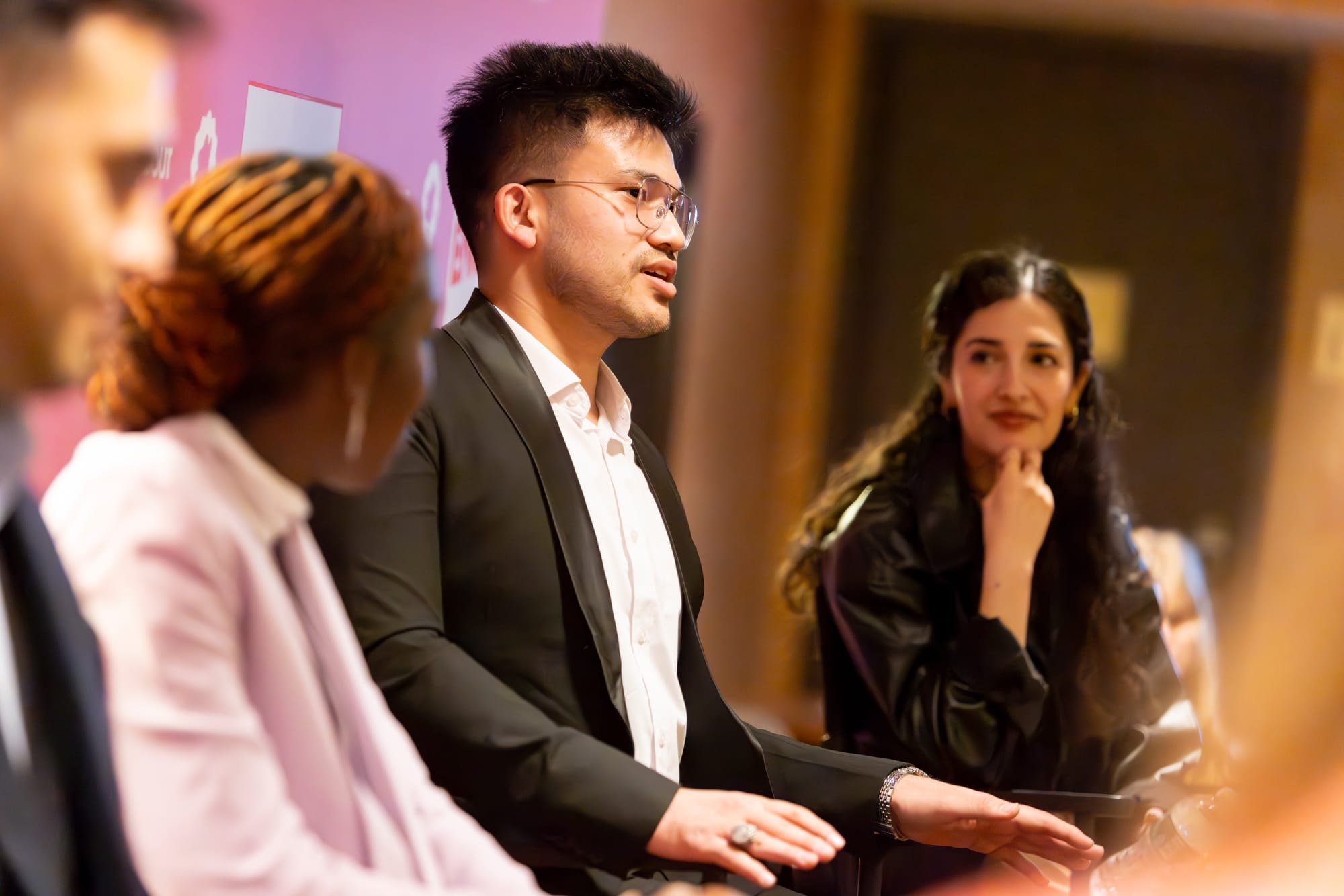 A man holds his hands up and speaks to the audience; a woman to his right looks on as he speaks. 