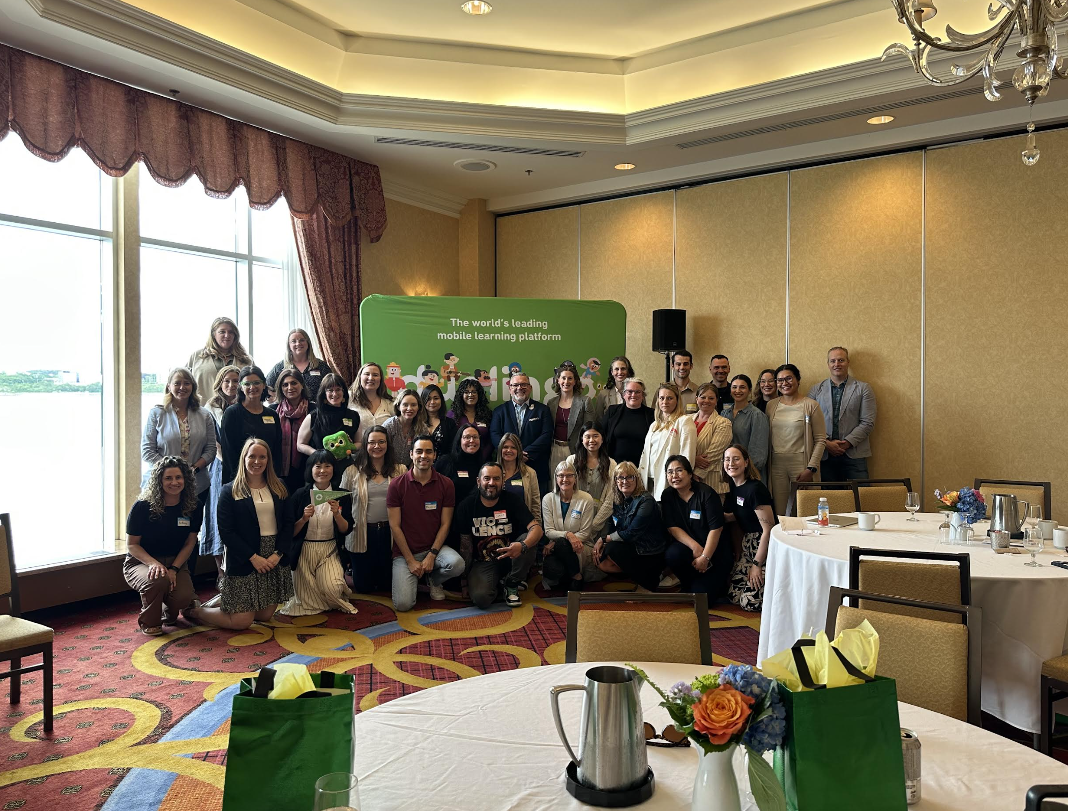 A group of more than 30 people standing together facing the camera, against a green backdrop that says "the world's leading mobile learning platform"